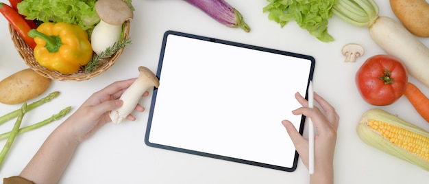 Young woman looking recipe on blank screen tablet while preparing ingredient for cooking with fresh vegetables