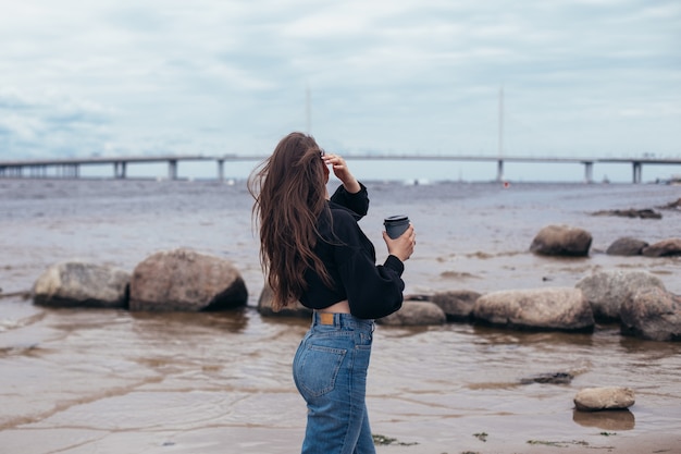 海を見て、コーヒーを飲む若い女性