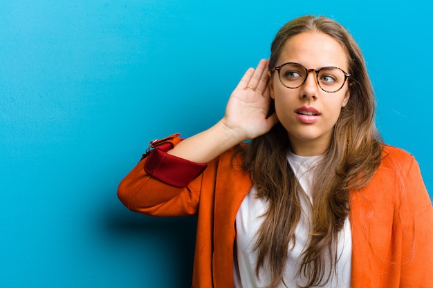 Young woman looking serious and curious, listening, trying to hear a secret conversation or gossip, eavesdropping on blue