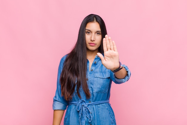 Young woman looking serious, stern, displeased and angry showing open palm making stop gesture