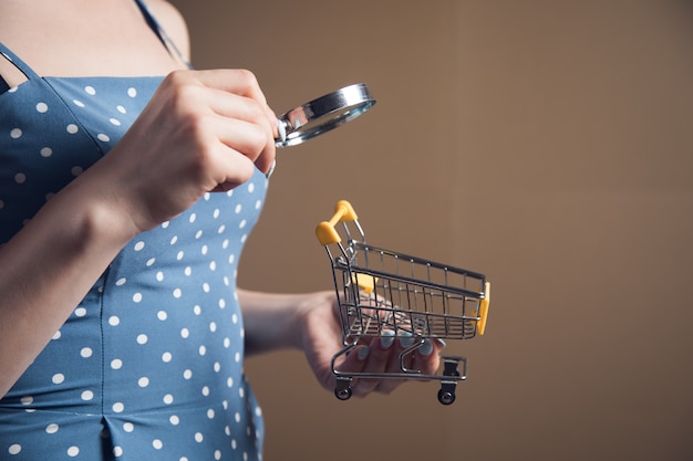 Young woman looking at a shopping cart with a magnifying glass. web search concept