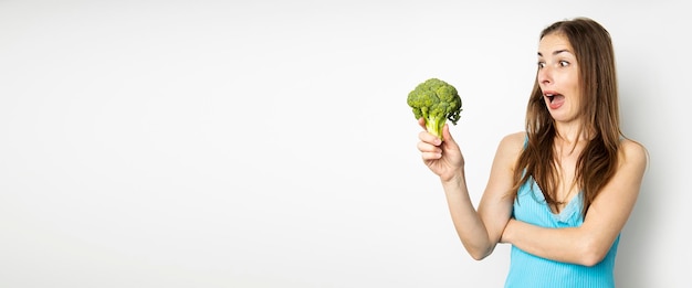 Young woman looking surprised at fresh broccoli on white background Banner