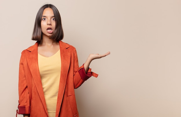 Young woman looking surprised and shocked, with jaw dropped holding an object with an open hand on the side