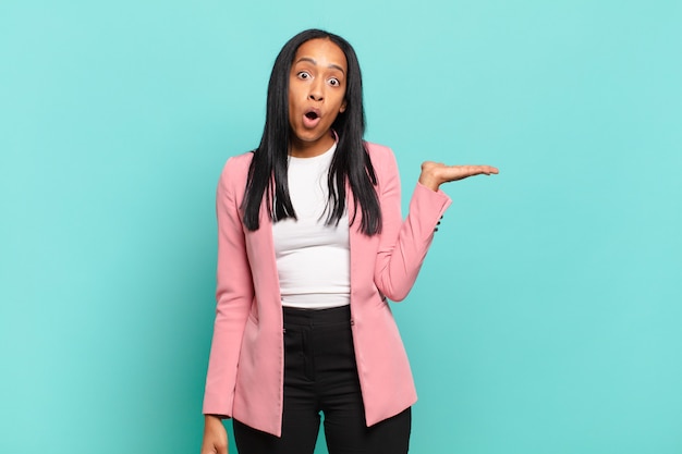 Young woman looking surprised and shocked, with jaw dropped holding an object with an open hand on the side