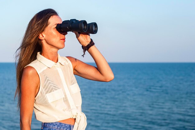 崖から海で双眼鏡を通して見ている若い女性