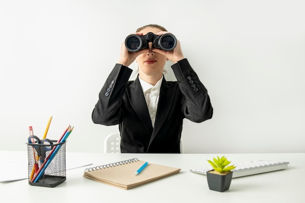 Young woman looking through binoculars while sitting at desk at workplace