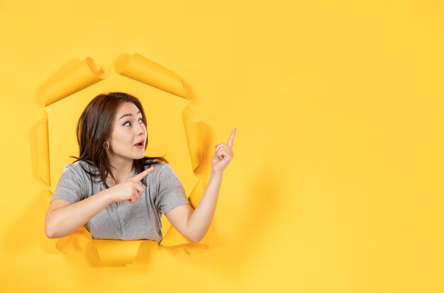 Photo young woman looking through a hole in yellow paper surface look window advertising