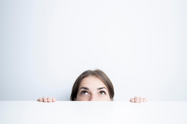 Photo young woman looking up from under a white table against a white wall