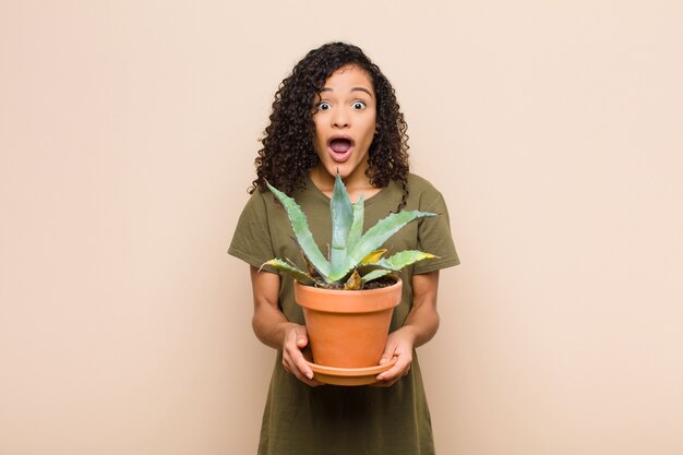 Young woman looking very shocked or surprised, staring with open mouth saying wow holding a cactus