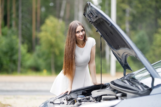 若い女性が故障した彼の車のボンネットの下を見る