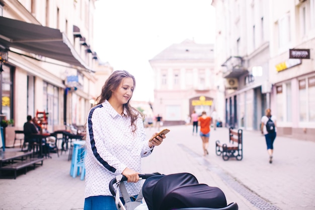 Foto la giovane donna guarda nel suo smartphone e cammina con un passeggino nel centro della città