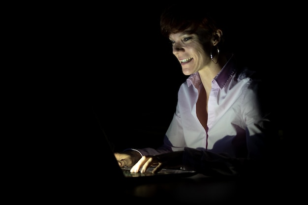 Young woman looks into laptop in dark room