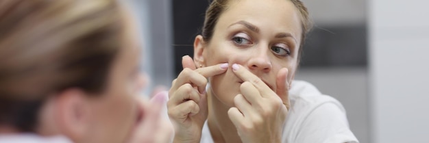 Young woman looks in the mirror and squeezes out a pimple