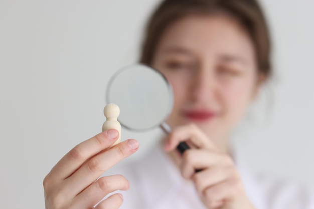 Young woman looks at small wooden figurine in hand through loupe female person examines human