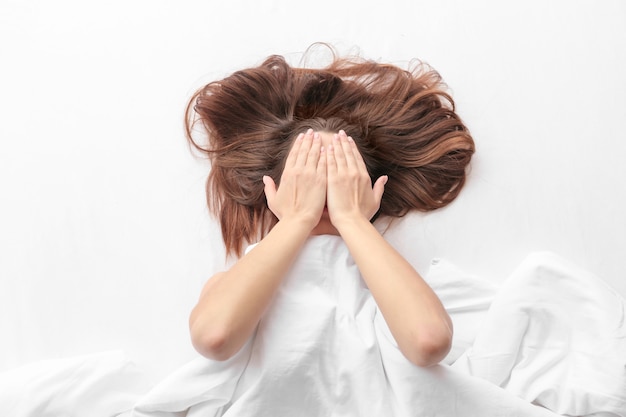 Young woman lying in bed and covering face with hands