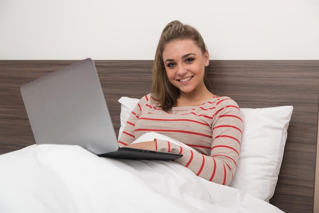 Young Woman Lying On Bed And Having Fun With Laptop In Bedroom