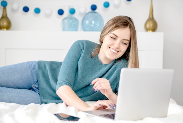 Young woman lying on bed using laptop. High quality photo