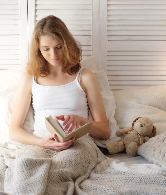 Photo young woman lying in bed while reading a book