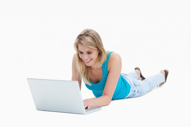 Молодая женщина, лежа на полу с ноутбуком