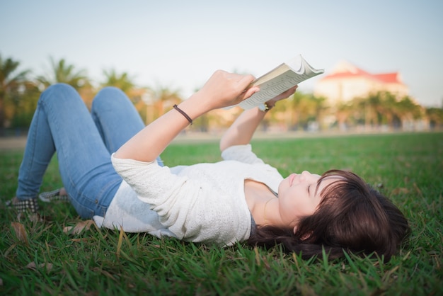 Foto una giovane donna sdraiata sull'erba e leggendo un libro