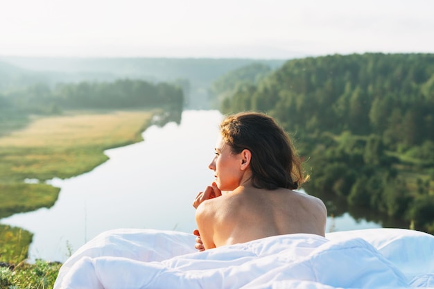 Фото Молодая женщина лежит в постели с белым постельным бельем на природе на фоне красивого пейзажа рано утром