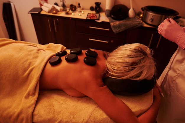 Young woman lying on massage table during hot stone massage session at SPA