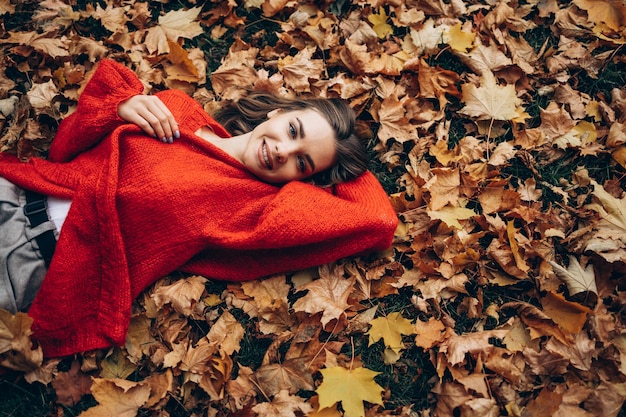 Foto giovane donna sdraiata nel parco sull'erba in foglie d'autunno