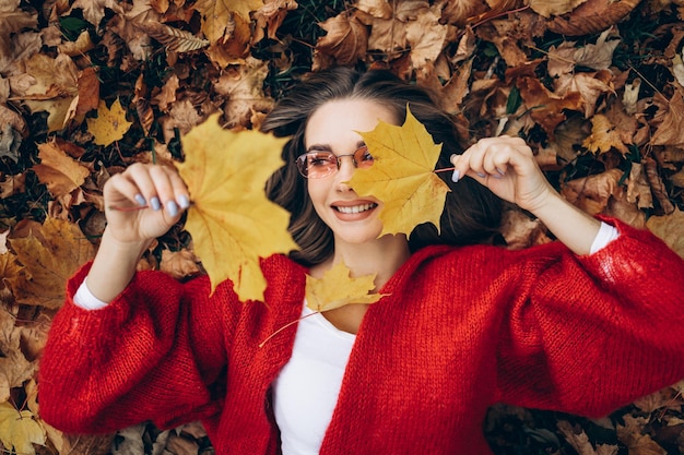 秋の紅葉の公園で芝生の上に横たわる若い女性