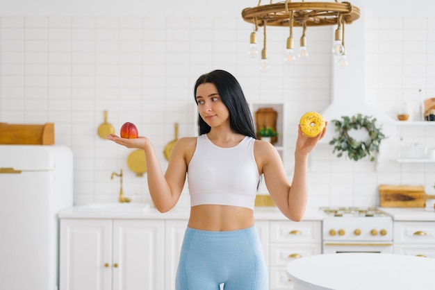 Молодая женщина делает выбор между персиком и пончиком Концепция диеты и здорового питания