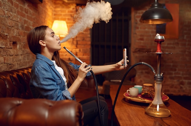 Young woman makes selfie with hookah in bar, mesmerizing cloud