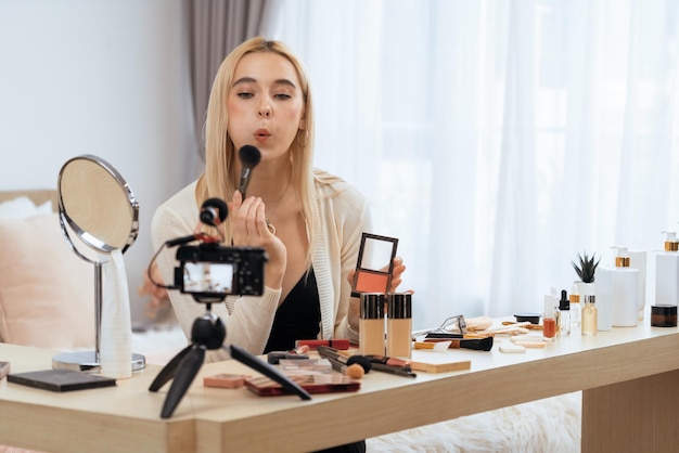 Young woman making beauty and cosmetic tutorial video content for social media Beauty blogger smiles to camera while showing how to apply mascara to audience or followers Blithe