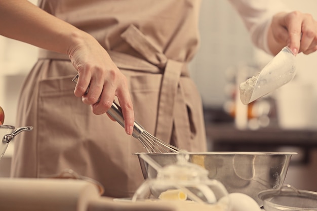 Young woman making dough in kitchen, closeup