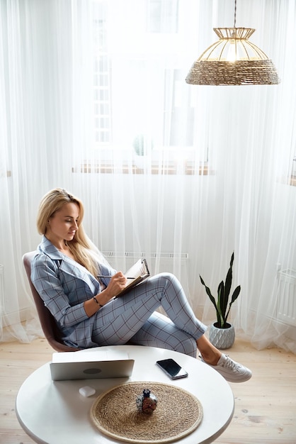 Young woman making notes in notebook sitting at workplace at home remote work