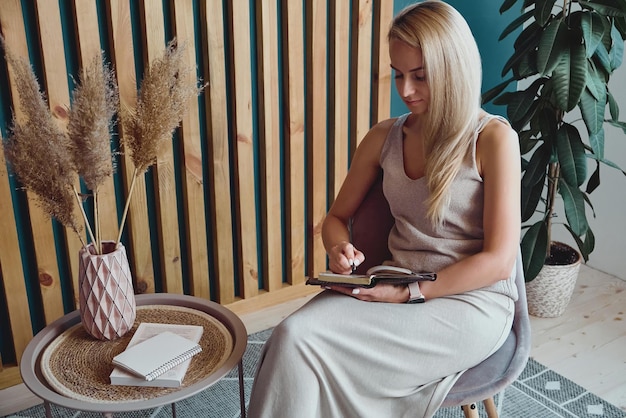 Young woman making notes in notebook sitting at workplace at home remote work