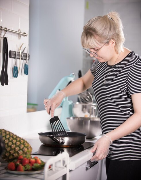 明るくモダンなキッチンでパンケーキを作る若い女性