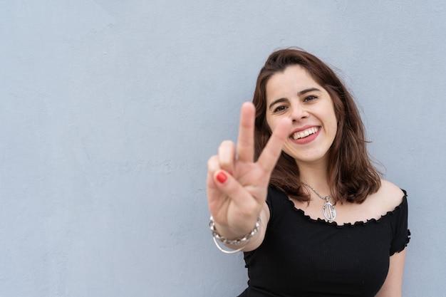 Giovane donna che fa il segno della pace con la mano e sorride.