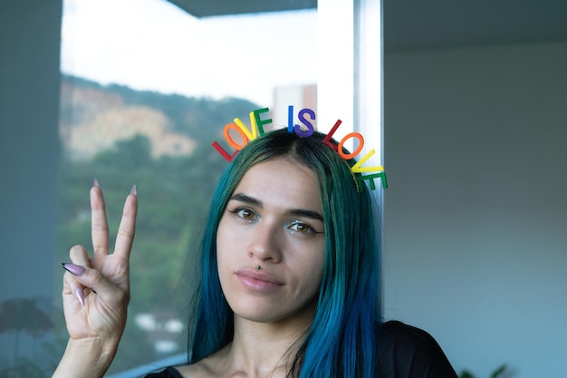 Young woman making victory sign with her hand LOVE IS LOVE headband Gay theme