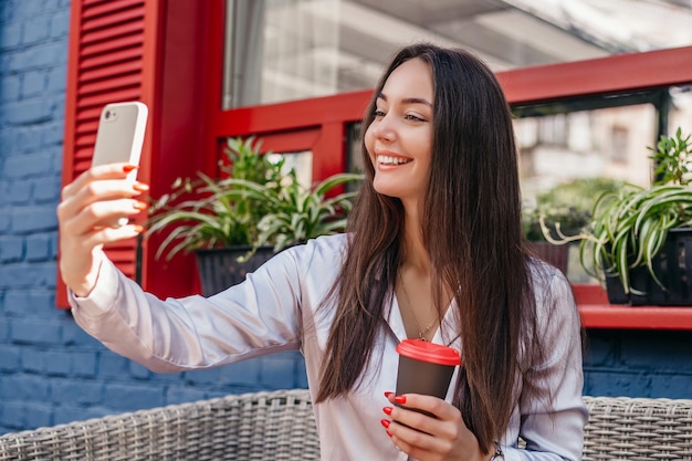 Giovane donna che fa una videochiamata e agita la mano nel suo smartphone