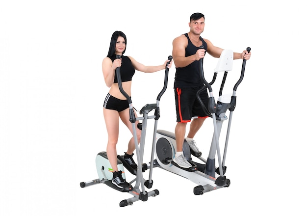 Young woman and man doing exercises on elliptical cross trainer