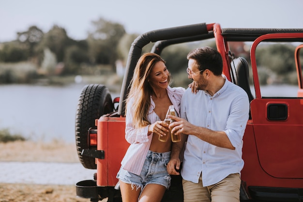 Photo young woman and man having fun outdoor near red car at summer day