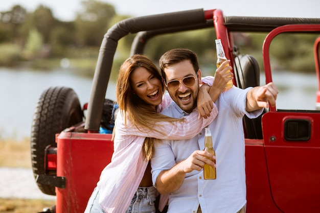 Young woman and man having fun outdoor near red car at summer day