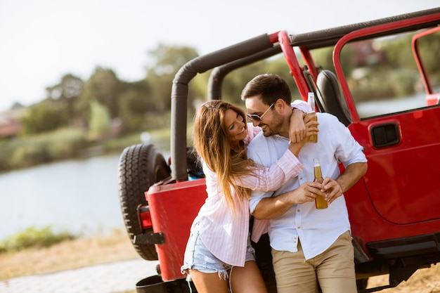 Young woman and man having fun outdoor near red car at summer day