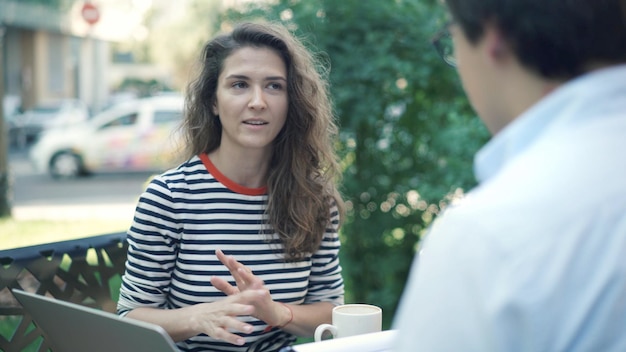 Young woman and man informal discussing business at the city cafe outdoors