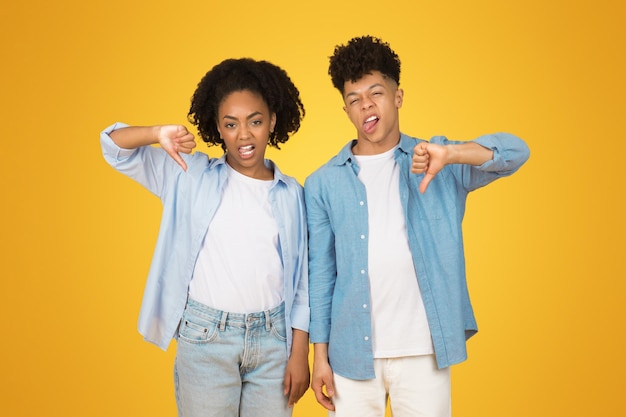 A young woman and man stand side by side giving thumbs down gestures with displeased expressions