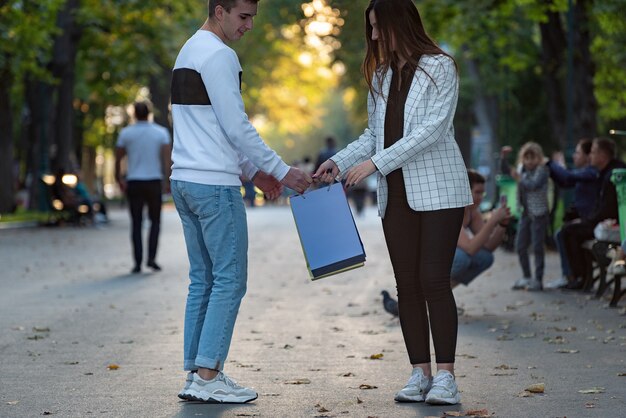 Photo young woman and man walking in park and holding shopping bag.