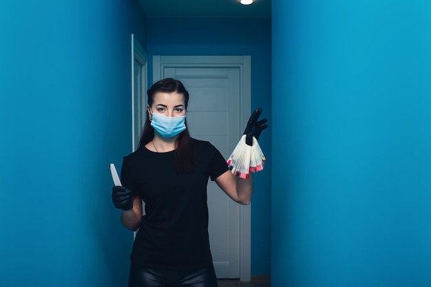 A young woman manicurist in a mask holds samples of colored nails and a nail file