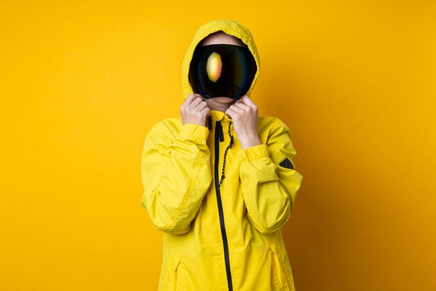 Young woman in a mask of cyberpunk goggles in a yellow jacket on a yellow background