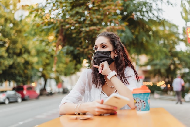 ウイルスのマスクをした若い女性がコーヒーを飲みに行きました。市は検疫中です。高品質