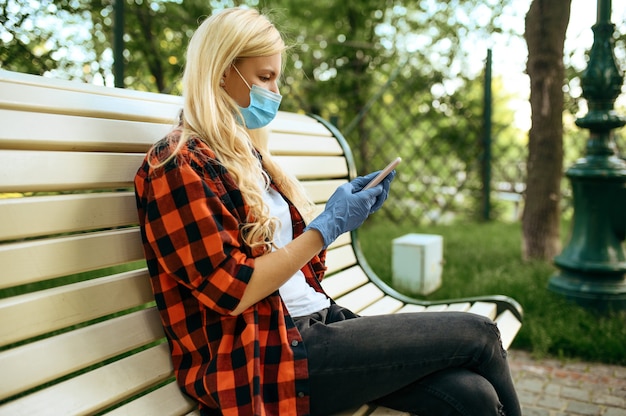 Young woman in mask sitting on bench in park, quarantine. Female person walking during the epidemic, health care and protection, pandemic lifestyle