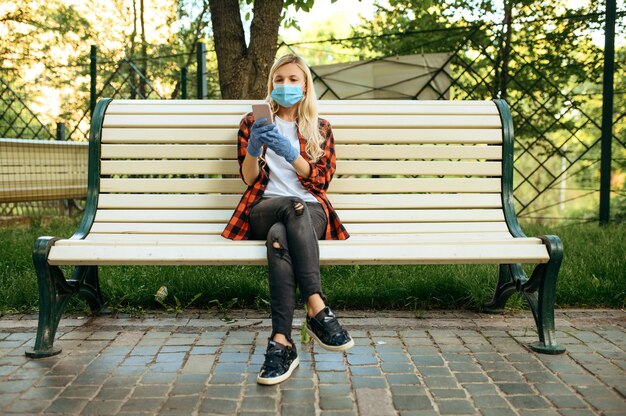 公園、検疫のベンチに座っているマスクの若い女性